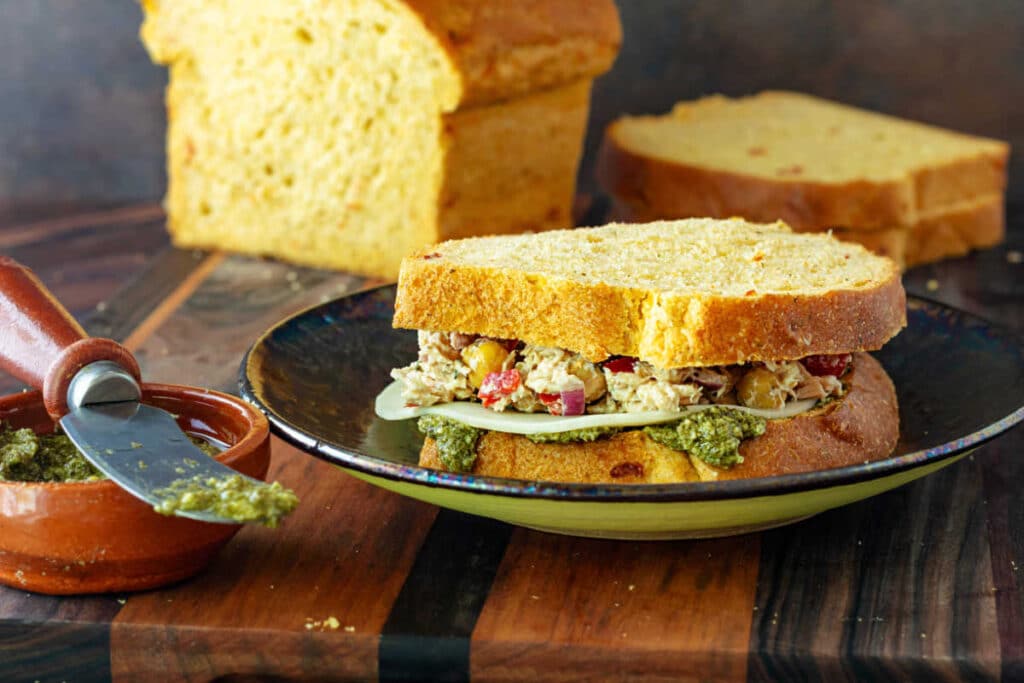 A tuna, pesto, and cheese sandwich built on sun-dried tomato pesto sandwich bread with some of the uncut loaf in the background.