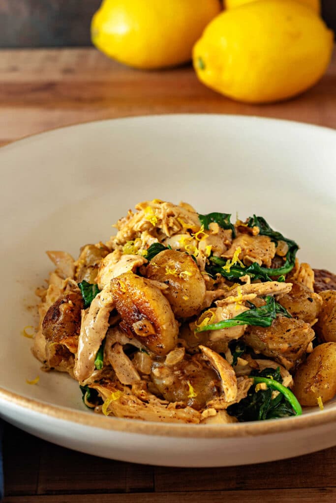 Bowl of golden pan-roasted gnocchi with shredded chicken, spinach, lemon zest, and creamy lemon sauce.