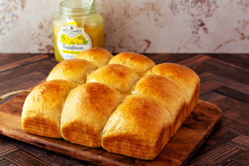 A freshly baked flat of 9 bountiful and soft honey wheat rolls on a cutting board.