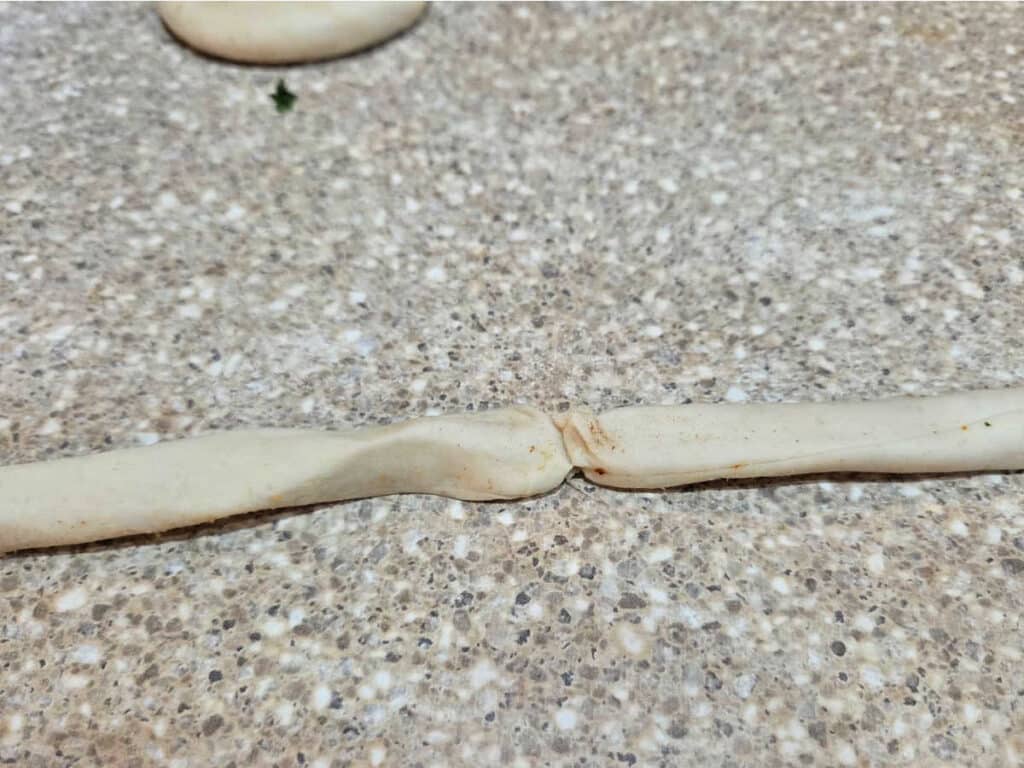 Flatbread dough rope broken in the middle during shaping, showing that small tears and breaks can happen while stretching the dough.