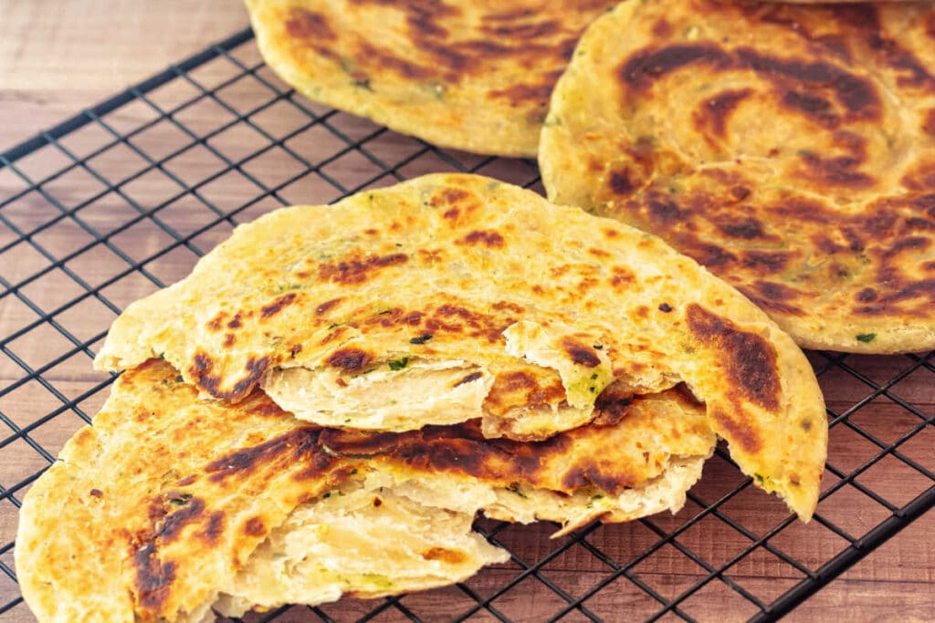 Golden-brown layered skillet flatbreads on a cooling rack, showing crisp surfaces and flaky interior layers.