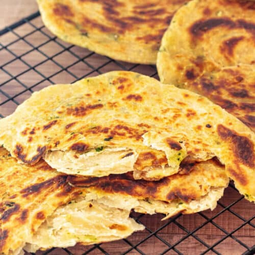 Golden-brown layered skillet flatbreads on a cooling rack, showing crisp surfaces and flaky interior layers.