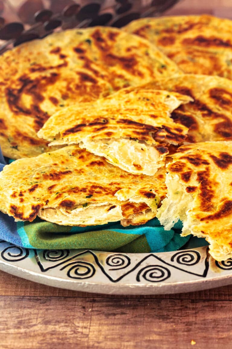 Flaky layered skillet flatbreads stacked on a platter, with one torn open to reveal crisp, pull-apart layers inside.