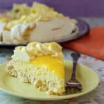 A slice of lemon pavlova decorated with lemon whipped cream and topped with bright yellow lemon curd.