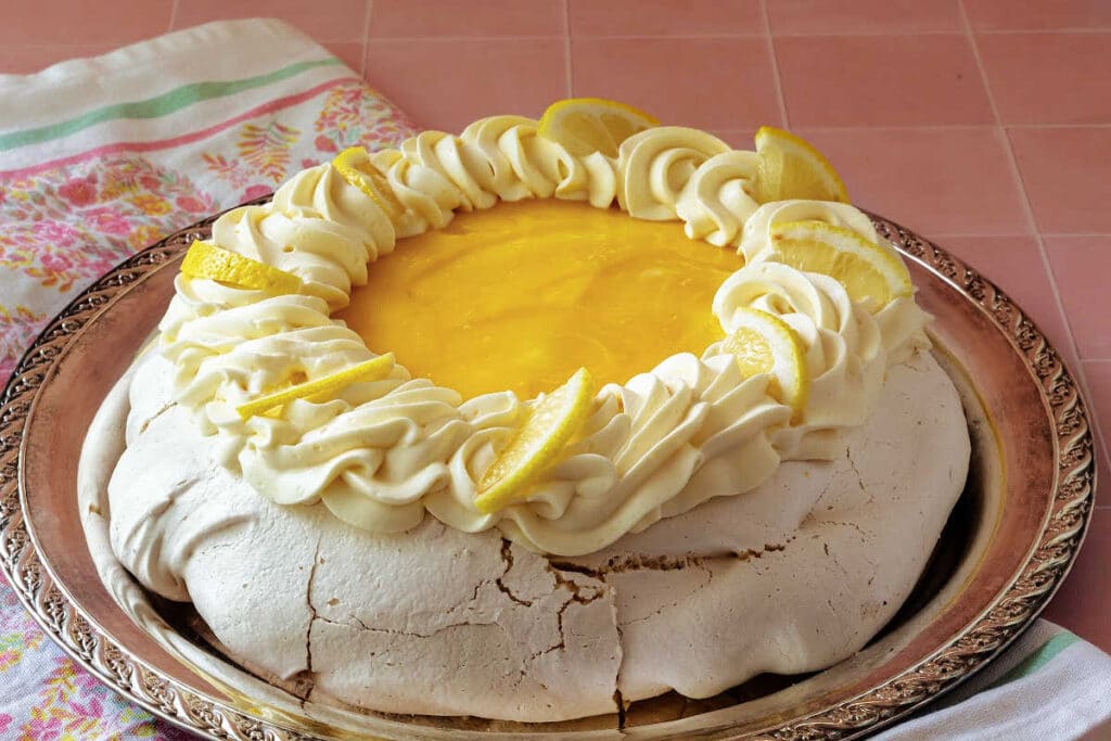 A pavlova on a silver platter with brilliant lemon curd on top and garnished with lemon whipped cream.