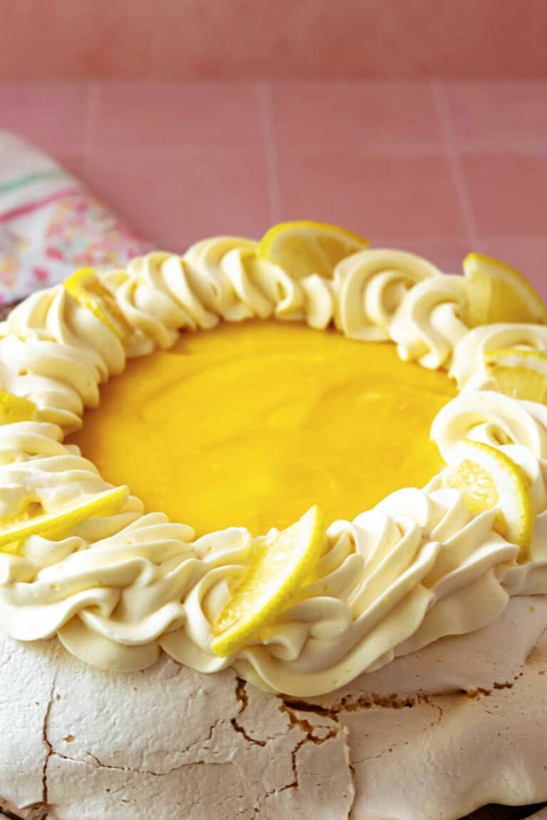 A generous lemon pavlova decorated with lemon whipped cream and quartered lemon slices.