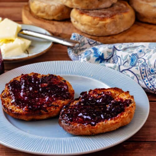 A split and toasted English muffin with melted butter and blueberry jam.