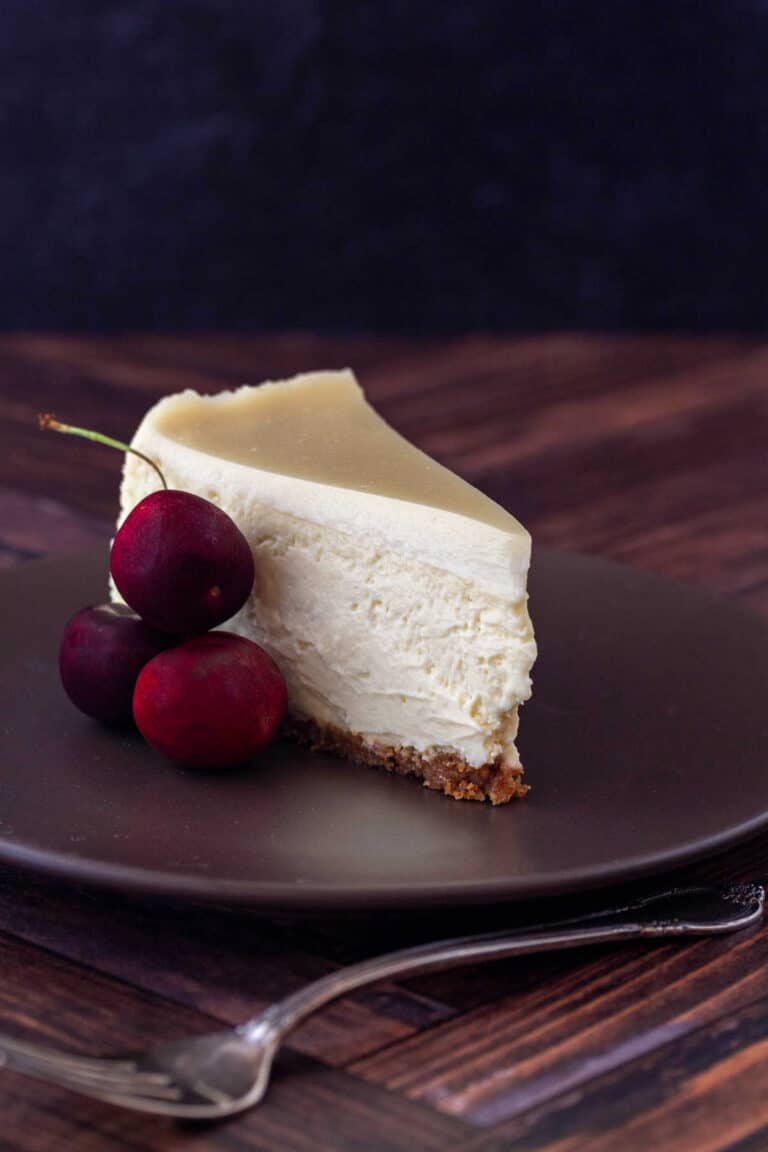 A slice of cheesecake with a sweetened sour cream topping and a Graham cracker crust on a brown plate.