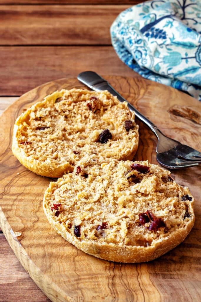 A fork-split cinnamon raisin English muffin on a cutting board. There are lots of nooks and crannies in the muffin and it is studded with plump dried fruit.