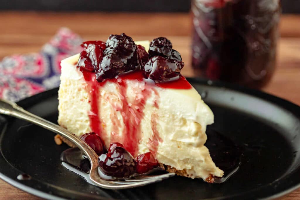 A slice of cherry cheesecake with spiced cherry preserves on top and the juices cascading down the sides.