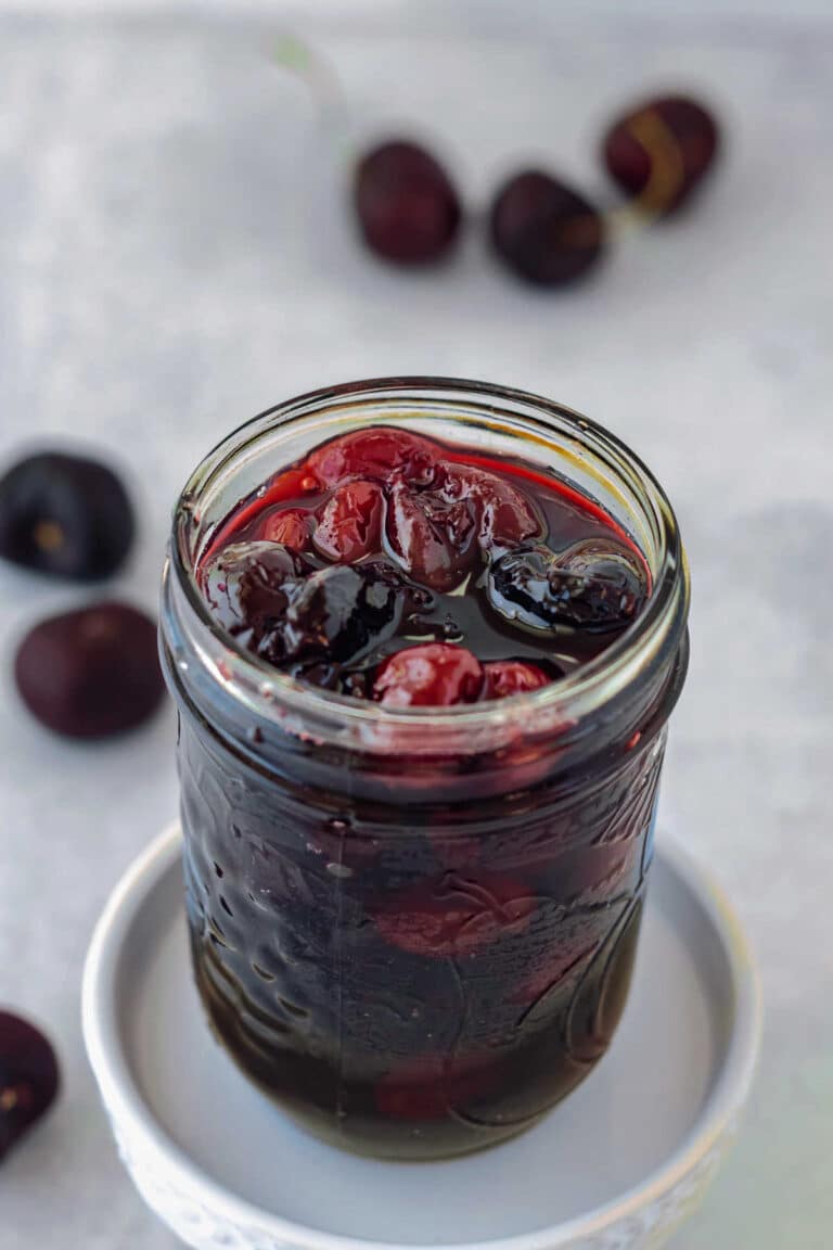 A glass jar of cherry pie preserves with some cherries scattered around.