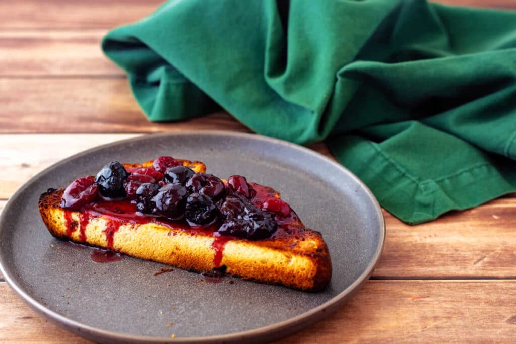 A toasted slice of sweet bread slathered with cherry pie preserves. 