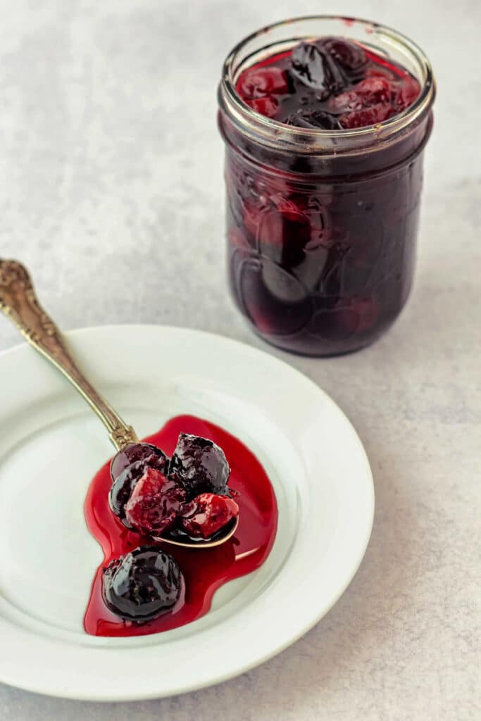 A spoonful of cherry preserves on a white plate with the syrup pooled in a bright cerise puddle.