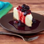 A slice of cheesecake topped with cherry pie preserves. The syrup is running down the sides of the slice and pooling on the plate.
