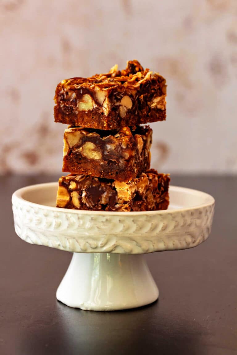 A stack of 3 peanut butter butterscotch magic bars on a small, white cupcake pedestal.