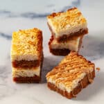 Several layered peanut butter coconut cookie bars on a marble surface.