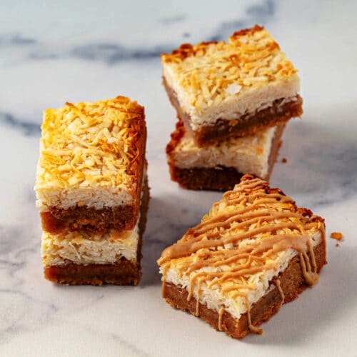 Several layered peanut butter coconut cookie bars on a marble surface.