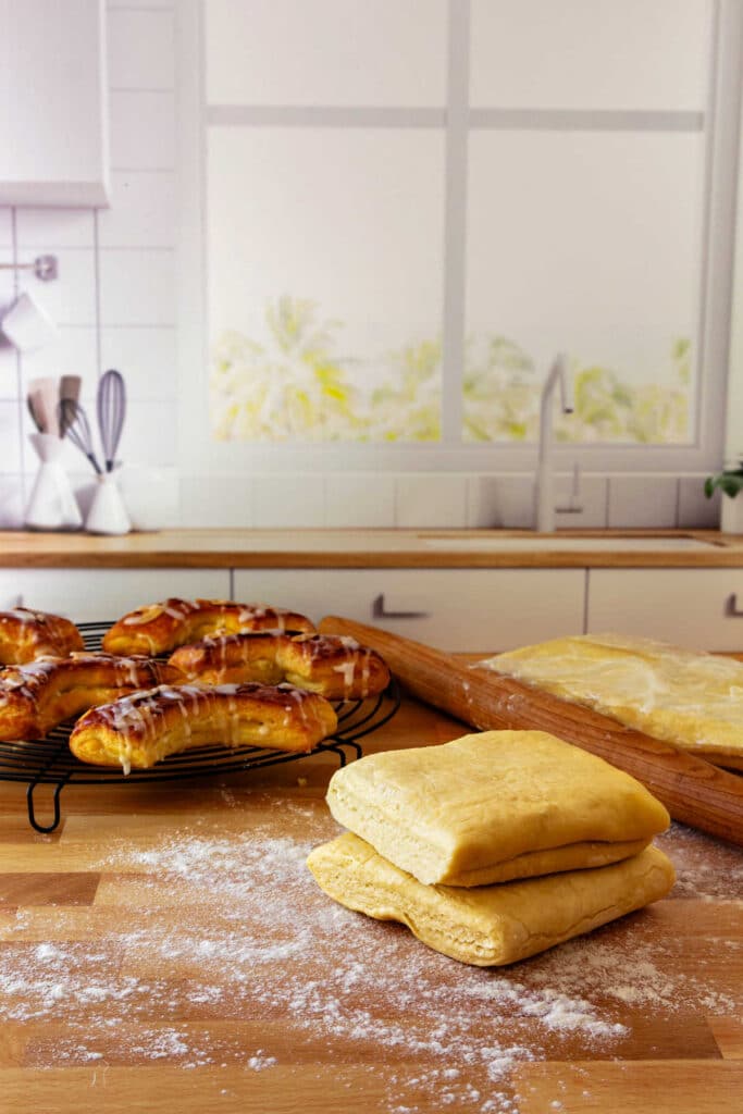 Blocks of Danish pastry on a floured board with baked bear claws in the background.