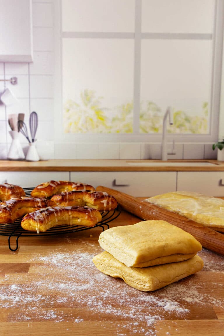 Blocks of Danish pastry on a floured board with baked bear claws in the background.