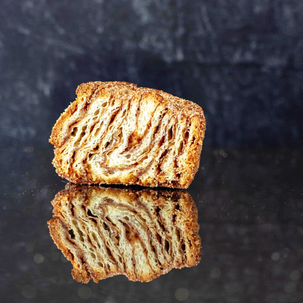 A morning bun sliced in half vertically to show the stripes of dough and spiced brown sugar filling.