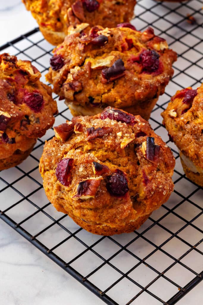 Cranberry pumpkin muffins with pecans cooling on a black, wire cooling rack.
