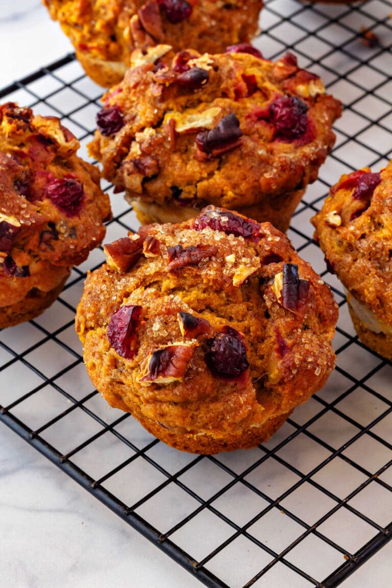 Cranberry pumpkin muffins with pecans cooling on a black, wire cooling rack.