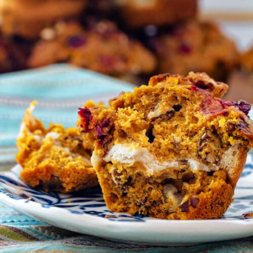 A cross section of a pumpkin muffin studded with chopped cranberries and pecans with a Greek yogurt ribbon running through the center.